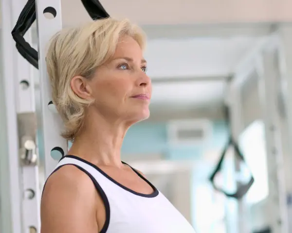 Mujer rubia en gimnasio, pensando en cómo tomar fat burner para mejorar su rutina de ejercicios.