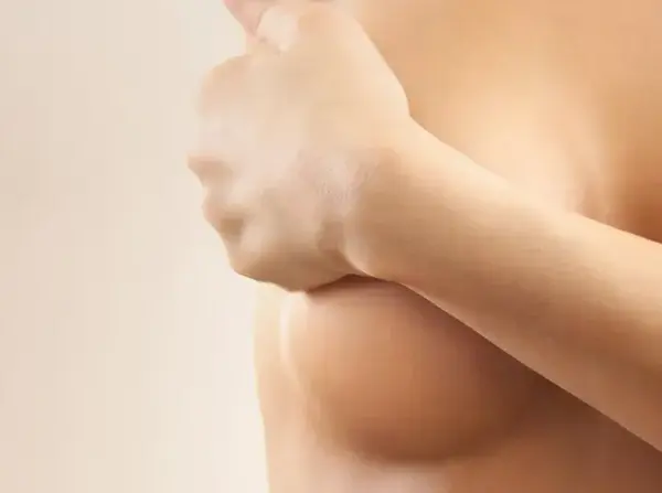 Una mujer se cubre los pechos con la mano, sintiendo un leve picor, un síntoma común en la menopausia.