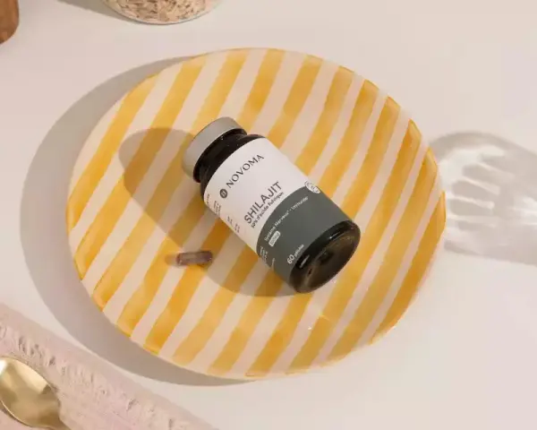 Un frasco de Shilajit y una cápsula sobre un plato rayado. Descubre para qué sirve el shilajit y cómo puede beneficiar tu sistema nervioso e inmunológico.