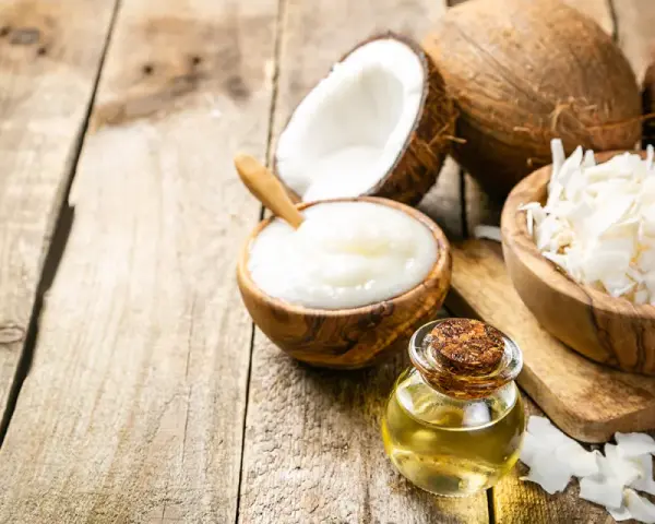 Aceite MCT en una botella junto a cocos partidos, crema de coco y coco rallado sobre madera rústica.