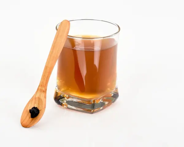 Vaso con bebida dorada y cuchara de madera con shilajit. Descubre los shilajit beneficios para la mujer.