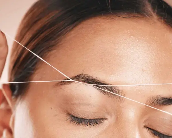 Detalle de depilación hilo en cejas. Una mano sostiene un hilo para perfilar la forma de la ceja, logrando un acabado preciso y natural.