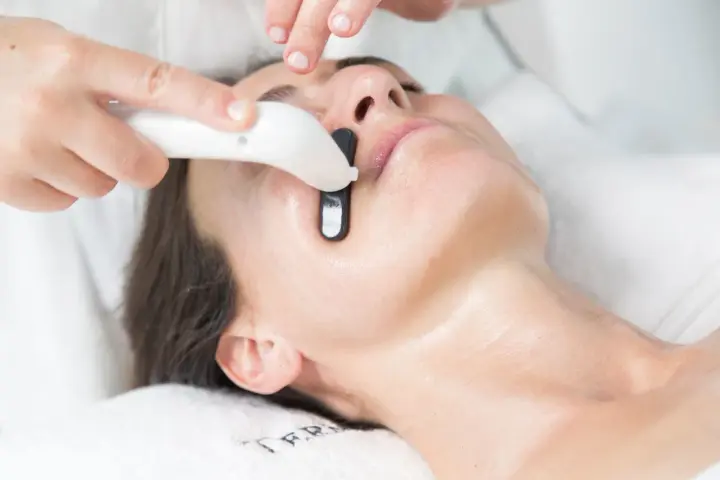 Una persona recibe un tratamiento facial en casa con un dispositivo que emite luz.