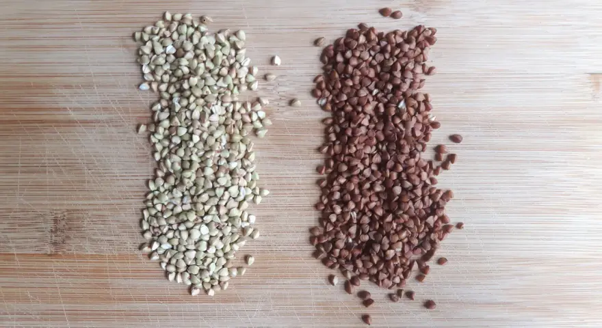 Dos montones de alforfón, uno verde y otro tostado, sobre una tabla de madera. ¿Alforfón que es? Un grano nutritivo.