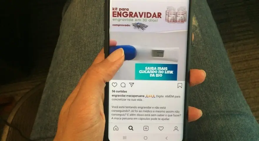 Mano sosteniendo un teléfono que muestra un anuncio de "kit para engravidar" y un test de embarazo. La maca peruana en cápsulas puede ayudar a quienes buscan el embarazo.