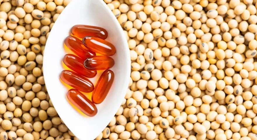 Cápsulas de lecitina de soja en un cuenco blanco sobre semillas de soja. La lecitina de soja tiene propiedades beneficiosas para la menopausia.