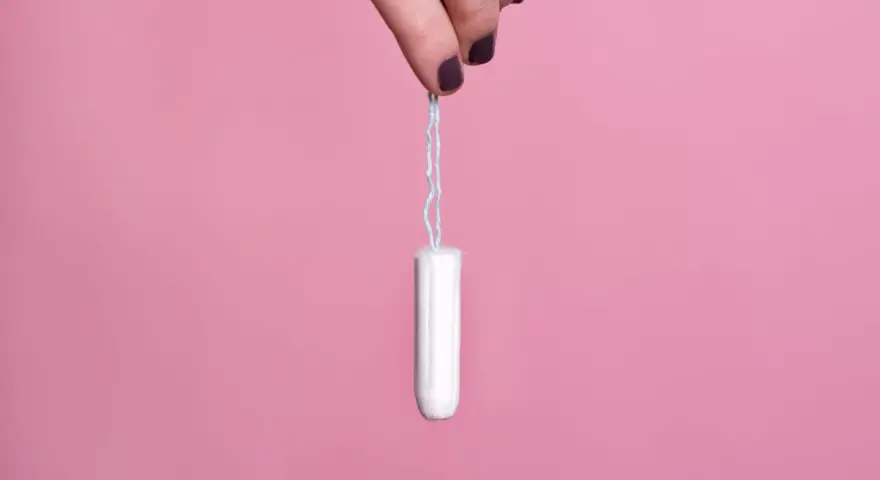 Mano sujetando un tampón blanco con hilo azul sobre fondo rosa. Existen diversos tipos de tampones para cada necesidad.