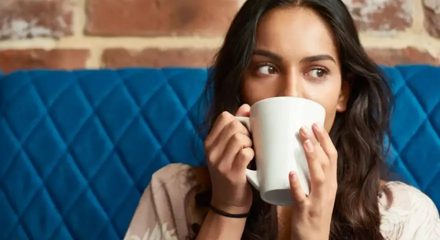Mujer con taza blanca, quizás probando una bebida sin cafeína para superar la abstinencia de cafeína.