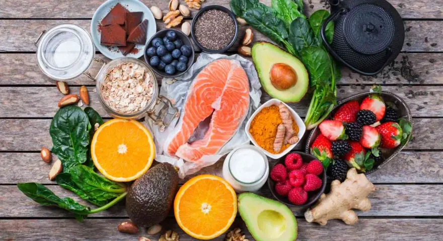 Salmón, bayas, aguacate, espinacas y cúrcuma son algunos de los alimentos antienvejecimiento que se muestran en esta composición sobre madera.