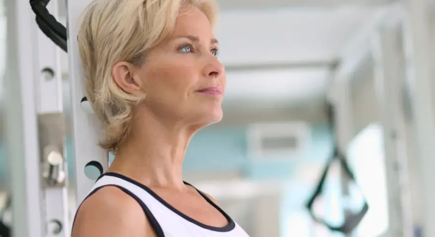 Mujer rubia en gimnasio, pensando en cómo tomar fat burner para mejorar su rutina de ejercicios.
