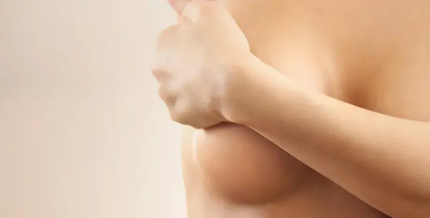 Una mujer se cubre los pechos con la mano, sintiendo un leve picor, un síntoma común en la menopausia.