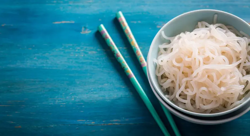 Un tazón de fideos konjac, ideal para una dieta saludable durante el embarazo, junto a palillos decorados sobre una mesa azul.