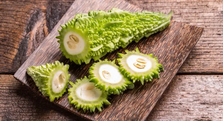 Melón amargo cortado en rodajas, mostrando sus semillas y pulpa blanca, sobre una tabla de madera rústica.