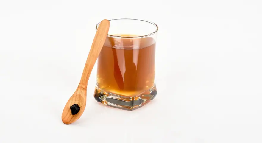 Vaso con bebida dorada y cuchara de madera con shilajit. Descubre los shilajit beneficios para la mujer.