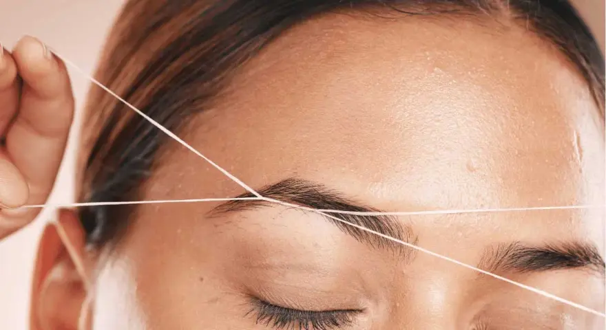 Detalle de depilación hilo en cejas. Una mano sostiene un hilo para perfilar la forma de la ceja, logrando un acabado preciso y natural.