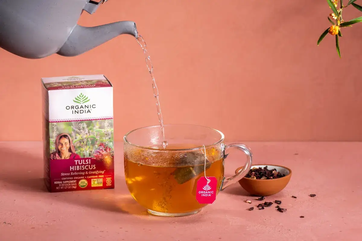 Agua caliente se vierte en una taza de t&eacute; de flor de jamaica, junto a una caja de t&eacute;.