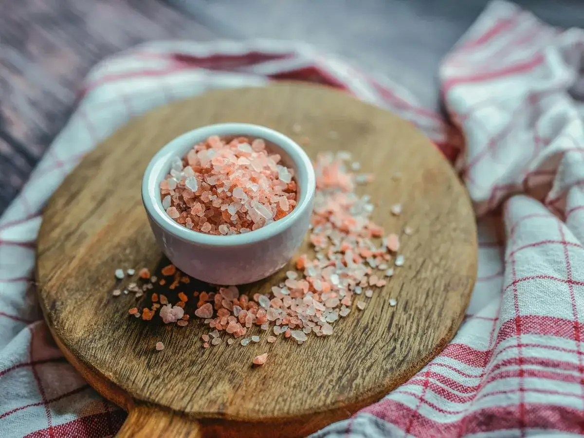 Sal del Himalaya en un cuenco, con granos esparcidos. Descubre sus beneficios y contraindicaciones.