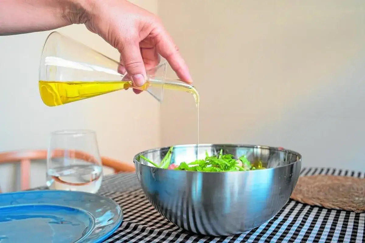 Mano vierte aceite de oliva, uno de los mejores superalimentos, sobre una ensalada fresca en un bol metálico.
