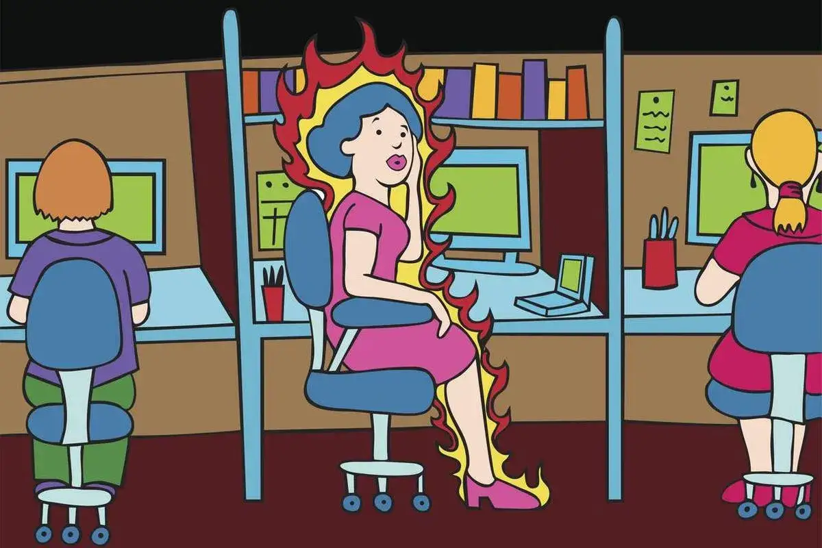 Mujer en oficina rodeada de llamas, como en testimonios menopausia. Otras dos mujeres trabajan a su lado.