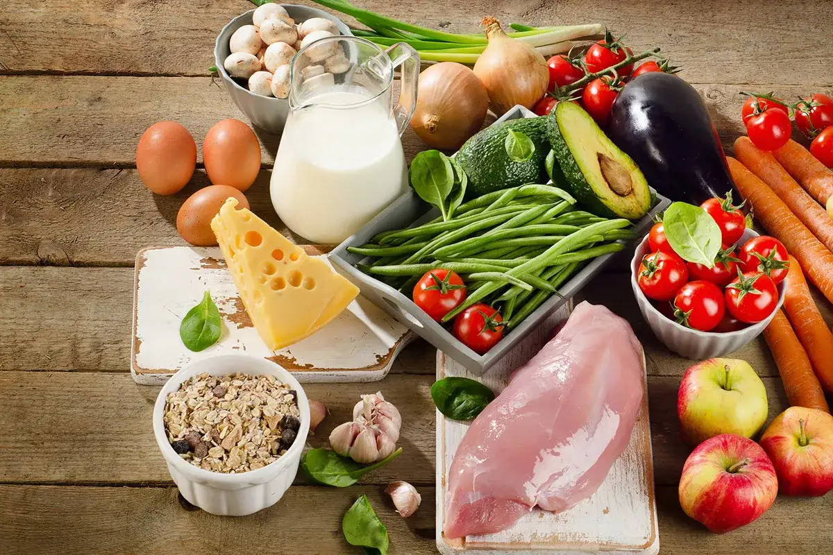 Variedad de alimentos antienvejecimiento: huevos, leche, queso, avena, pollo, aguacate, judías verdes, tomates, berenjena, zanahorias, champiñones, cebolla, ajo y manzanas.