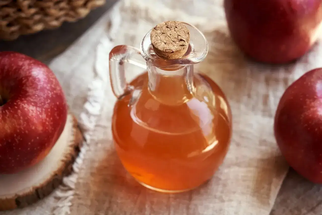 Vinagre de manzana en un frasco de vidrio, rodeado de manzanas rojas. Descubre los 10 beneficios del vinagre de manzana.