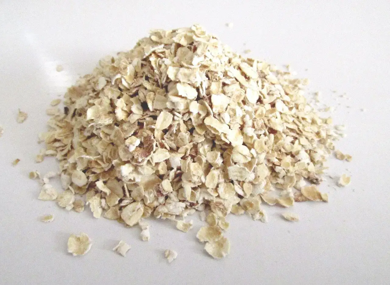 Mont&oacute;n de copos de avena sobre fondo blanco. Estos copos son el resultado de procesar el grano, mostrando de donde proviene la avena.