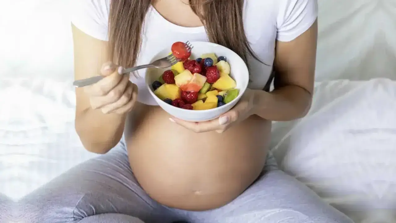Mujer embarazada disfrutando de una ensalada de frutas, una dieta saludable es clave para el desarrollo del bebé y para asegurar suficiente biotina y embarazo.