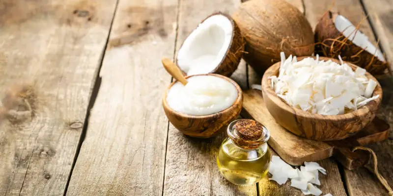Aceite MCT en una botella junto a cocos partidos, crema de coco y coco rallado sobre madera rústica.
